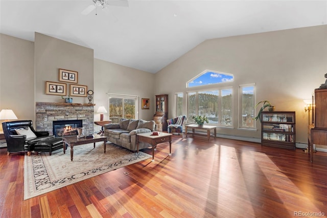 living room with high vaulted ceiling, ceiling fan, wood-type flooring, and a stone fireplace