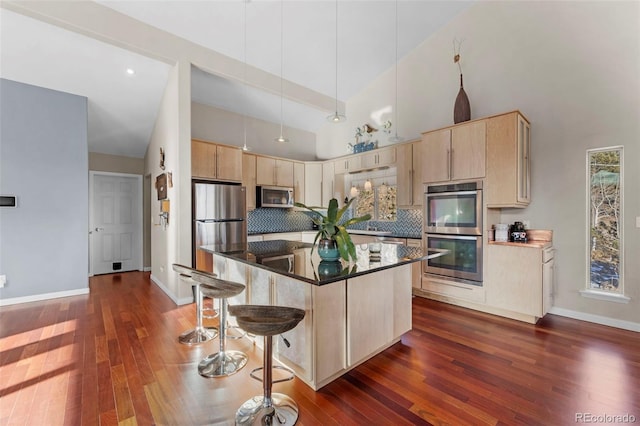 kitchen with stainless steel appliances, hanging light fixtures, a center island, a towering ceiling, and light brown cabinetry