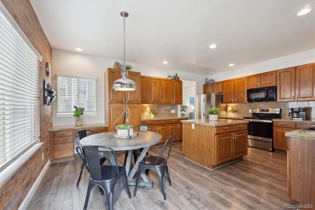 kitchen with a center island, brown cabinetry, light wood-style floors, backsplash, and appliances with stainless steel finishes