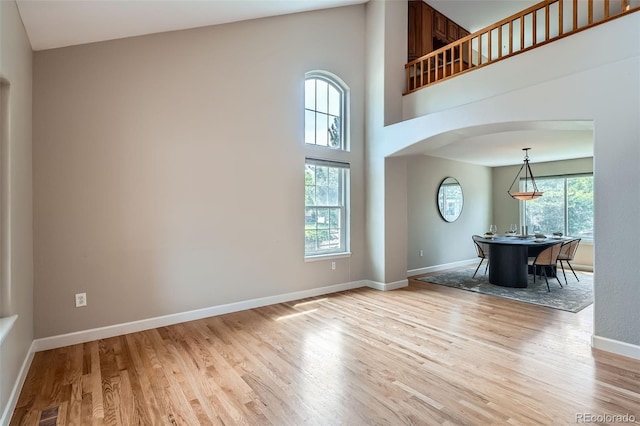 5784 W 81st Cir, Arvada, CO 80003 - unfurnished living room featuring arched walkways, light wood-style floors, baseboards, and a towering ceiling