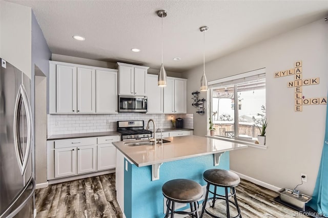 kitchen featuring appliances with stainless steel finishes, dark hardwood / wood-style flooring, sink, white cabinets, and hanging light fixtures