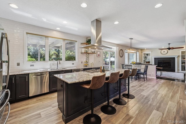 16498 E Lake Dr, Centennial, CO 80016 - kitchen with appliances with stainless steel finishes, island range hood, light wood-style floors, light stone countertops, and backsplash