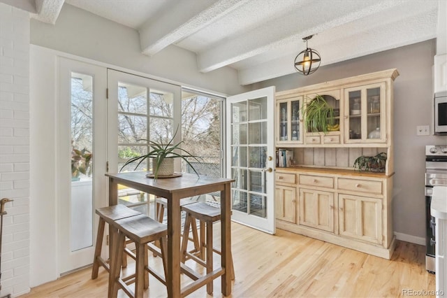 dining area featuring beamed ceiling, light wood-style flooring, a textured ceiling, and baseboards