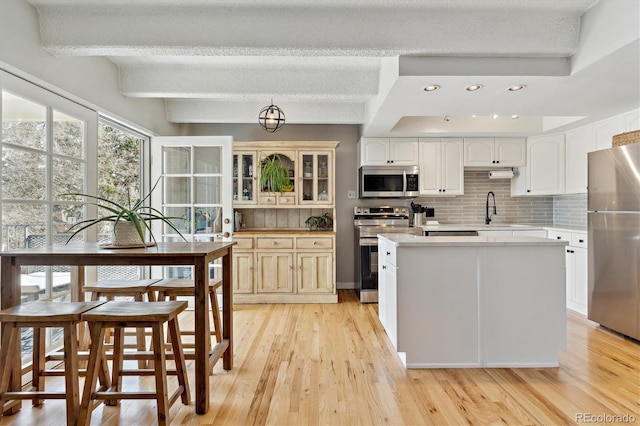 kitchen featuring tasteful backsplash, light countertops, appliances with stainless steel finishes, light wood-style floors, and a sink