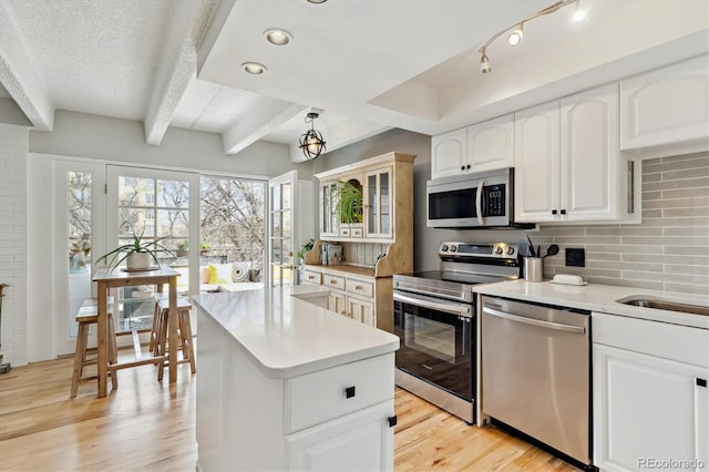 kitchen featuring beamed ceiling, a center island, stainless steel appliances, light wood finished floors, and decorative backsplash