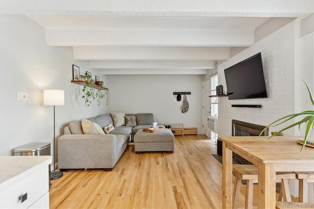 living room featuring beam ceiling, light wood-style flooring, and a fireplace