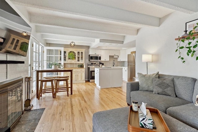 living area featuring beamed ceiling, light wood-style floors, and a fireplace