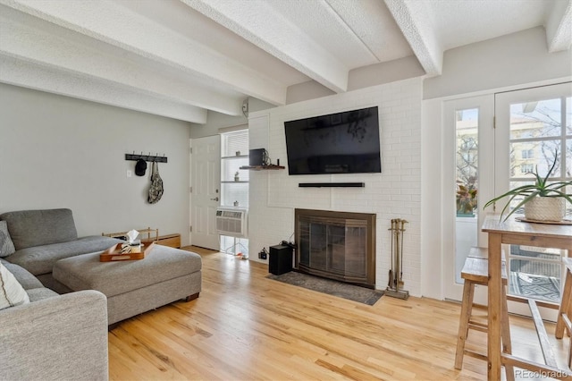 living room featuring beam ceiling, a wall mounted AC, a textured ceiling, a fireplace, and light wood finished floors