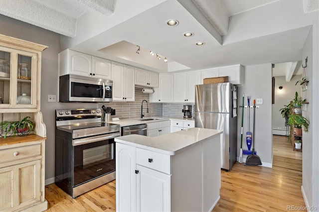 kitchen with a sink, stainless steel appliances, light countertops, decorative backsplash, and baseboard heating