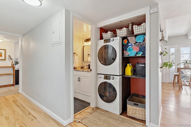 clothes washing area featuring laundry area, wood finished floors, stacked washer and clothes dryer, and baseboards