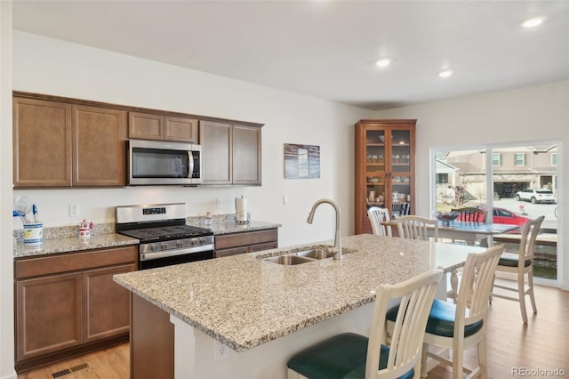 kitchen with light stone countertops, appliances with stainless steel finishes, light hardwood / wood-style floors, and sink