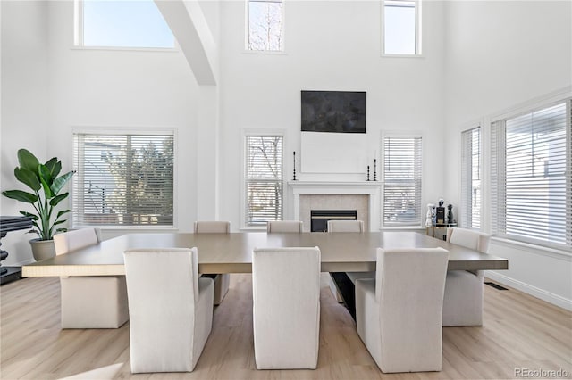 dining space with a tiled fireplace, a towering ceiling, and light hardwood / wood-style floors