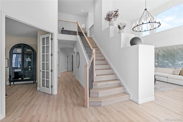 staircase with a towering ceiling, wood-type flooring, and a notable chandelier