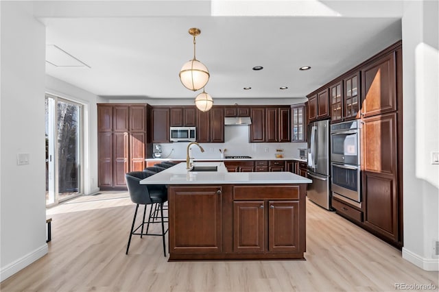 kitchen with sink, decorative light fixtures, a center island with sink, stainless steel appliances, and light hardwood / wood-style floors