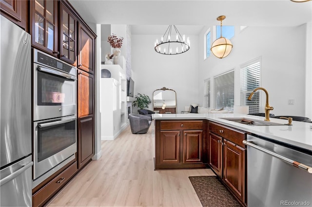 kitchen featuring decorative light fixtures, sink, a notable chandelier, stainless steel appliances, and light wood-type flooring