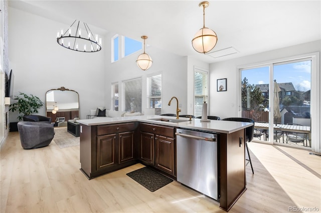 kitchen featuring sink, a breakfast bar area, light hardwood / wood-style floors, decorative light fixtures, and stainless steel dishwasher