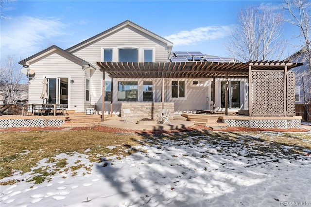 snow covered back of property featuring a wooden deck, a pergola, and a patio