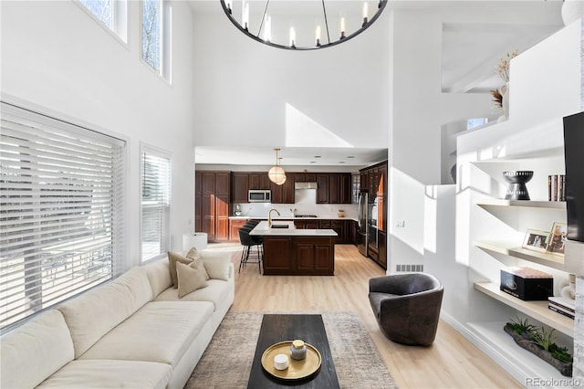 living room with sink, light hardwood / wood-style floors, a chandelier, and a high ceiling