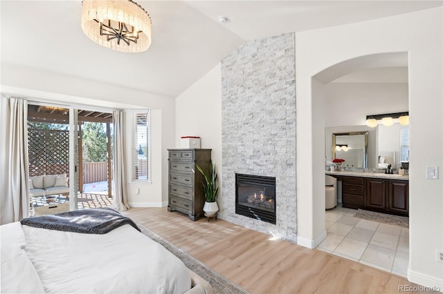 bedroom featuring ensuite bathroom, a stone fireplace, lofted ceiling, access to exterior, and light hardwood / wood-style flooring