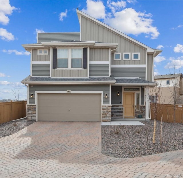 view of front of home featuring stone siding, decorative driveway, an attached garage, and fence