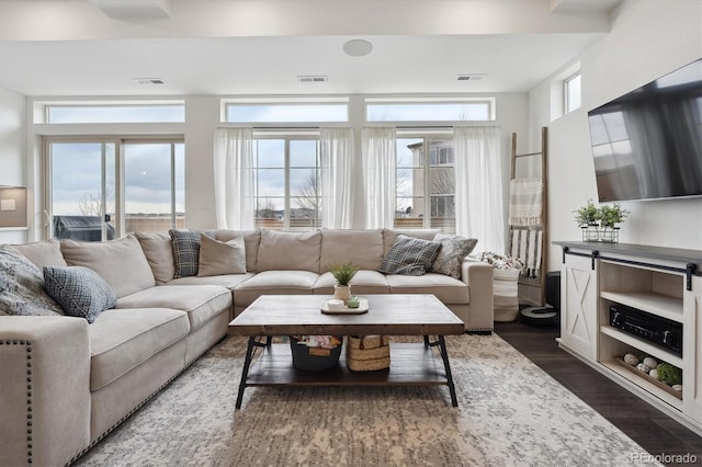 living area with dark wood-style flooring, visible vents, and a healthy amount of sunlight