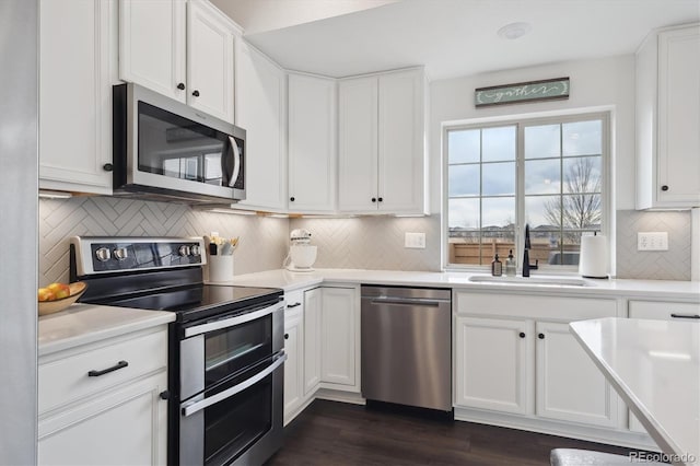 kitchen with white cabinets, appliances with stainless steel finishes, dark wood-style flooring, light countertops, and a sink