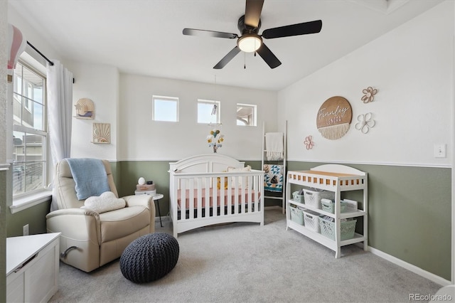 carpeted bedroom with a crib, ceiling fan, and baseboards