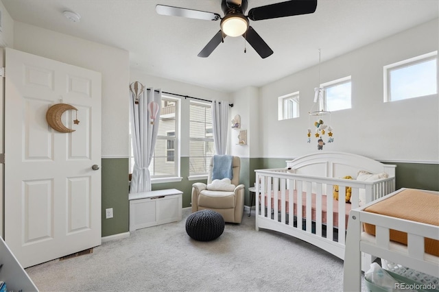 carpeted bedroom with a crib and ceiling fan