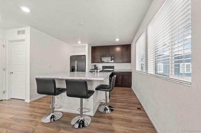 kitchen featuring a center island with sink, hardwood / wood-style floors, stainless steel refrigerator with ice dispenser, and a kitchen bar