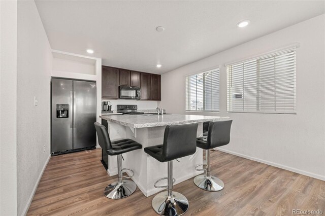 kitchen featuring dark brown cabinets, a kitchen island with sink, light hardwood / wood-style flooring, black appliances, and sink