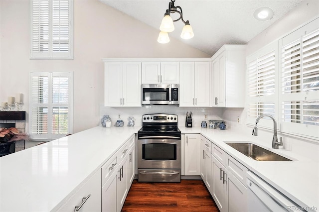 kitchen with appliances with stainless steel finishes, sink, white cabinets, hanging light fixtures, and lofted ceiling