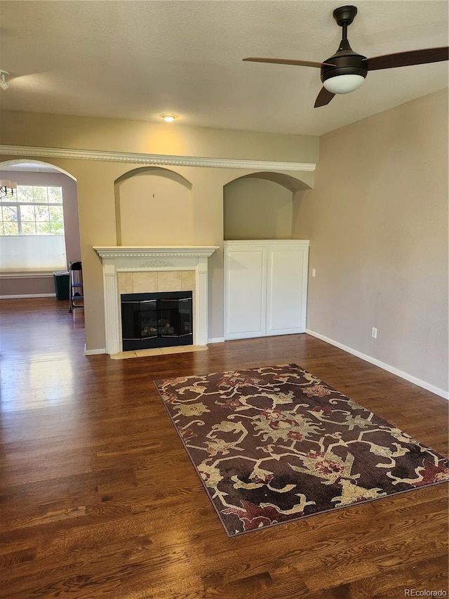 unfurnished living room with dark wood-type flooring, a tiled fireplace, and ceiling fan