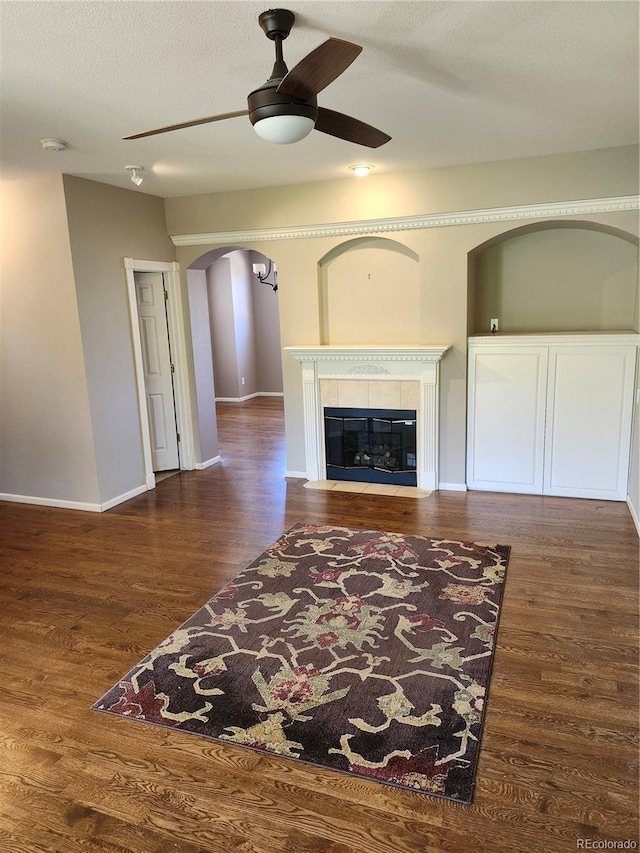 unfurnished living room with dark wood-type flooring, ceiling fan, a textured ceiling, and a fireplace