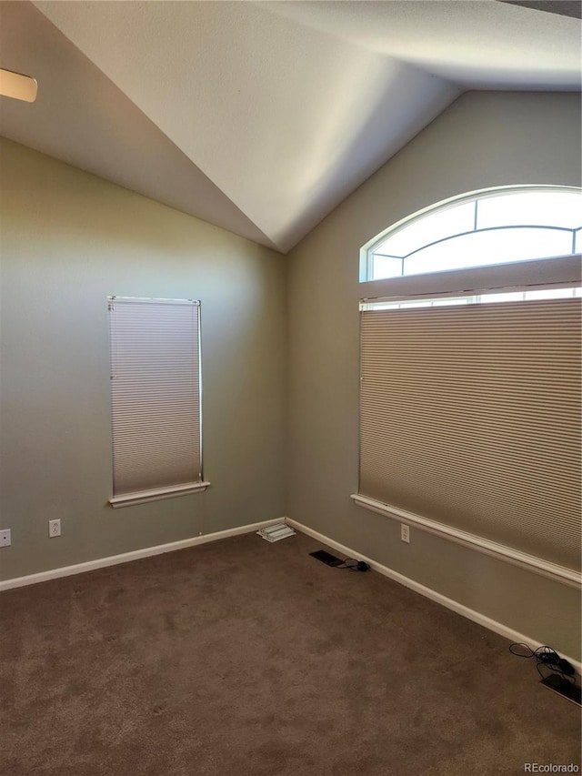 spare room featuring dark carpet and vaulted ceiling