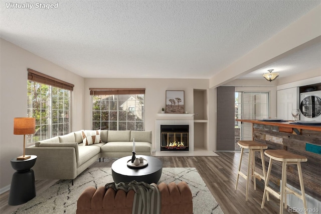 living room featuring a textured ceiling, stacked washer and clothes dryer, wood finished floors, and a tiled fireplace