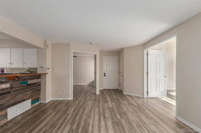 unfurnished living room with light wood-style flooring, a textured ceiling, and baseboards