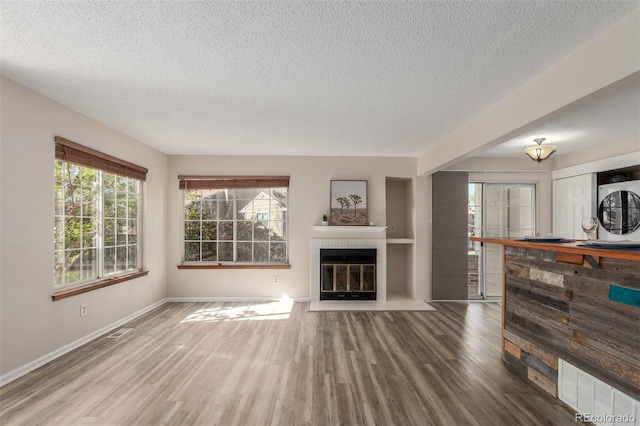 unfurnished living room featuring a textured ceiling, wood finished floors, a fireplace, and baseboards