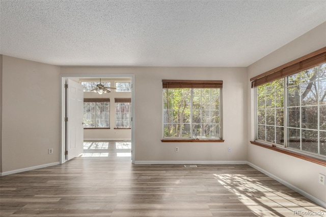 spare room featuring healthy amount of natural light, a textured ceiling, wood finished floors, and baseboards