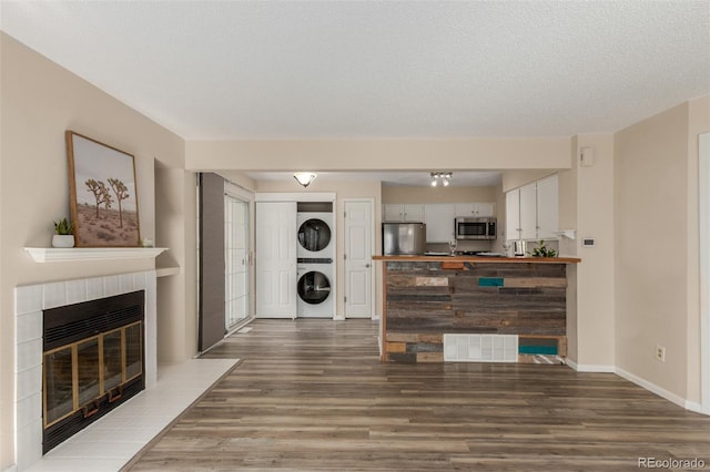 living area with estacked washer and dryer, wood finished floors, a tile fireplace, baseboards, and a textured ceiling