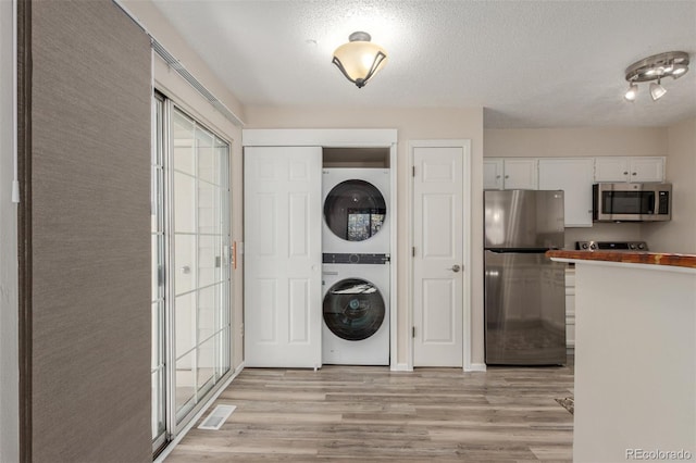 laundry area with estacked washer and dryer, light wood-type flooring, and a textured ceiling