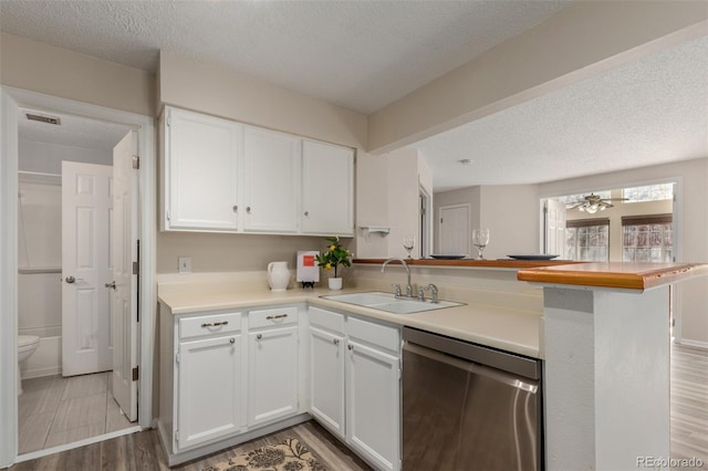 kitchen with dishwasher, a sink, a peninsula, a textured ceiling, and white cabinets