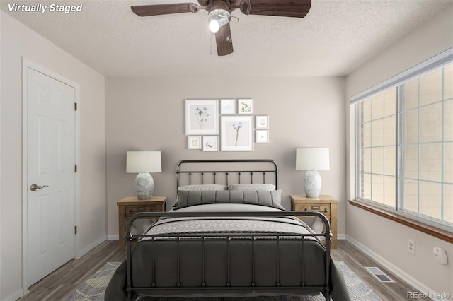 bedroom with dark wood-type flooring, a textured ceiling, multiple windows, and baseboards