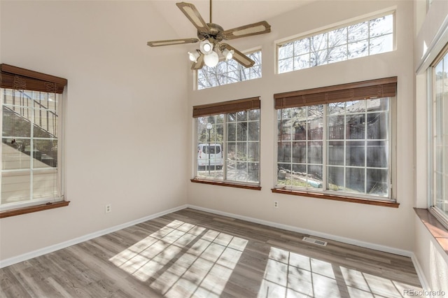 unfurnished room with a high ceiling, a ceiling fan, wood finished floors, and baseboards