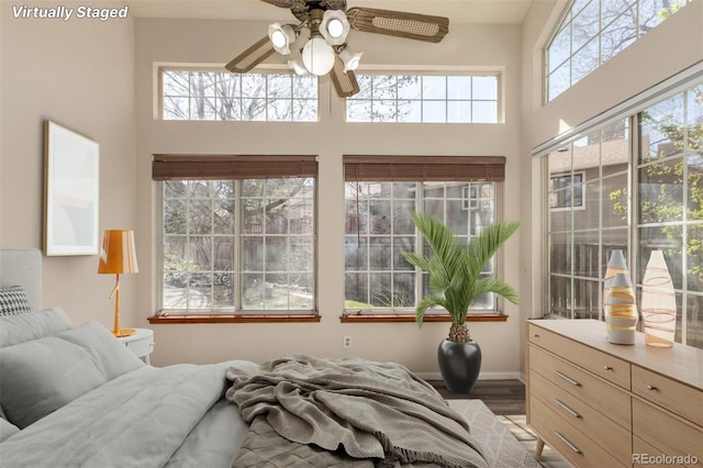 bedroom with a towering ceiling, wood finished floors, baseboards, and a ceiling fan