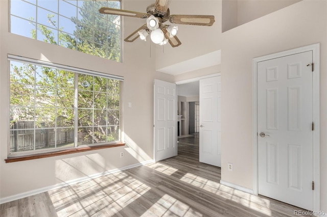 unfurnished dining area featuring a high ceiling, baseboards, ceiling fan, and wood finished floors