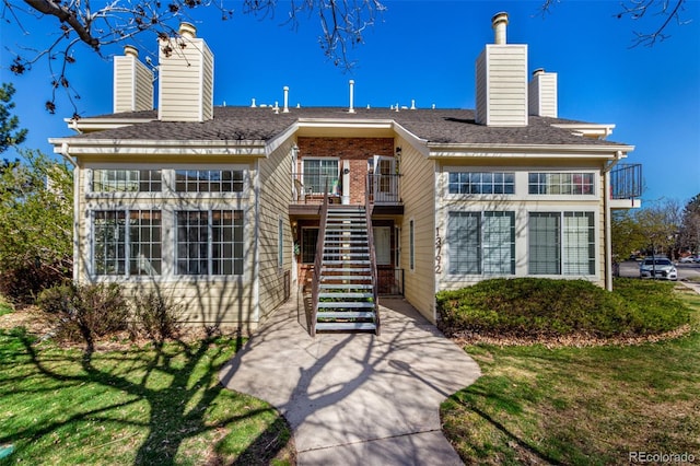 view of front of house with a chimney, stairs, a balcony, and a front yard