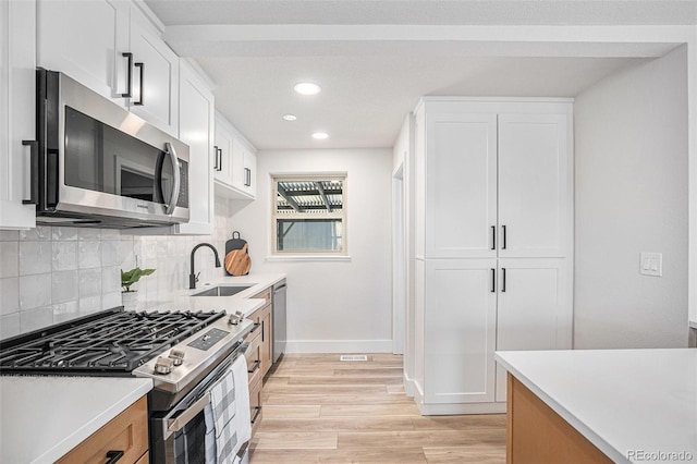 kitchen with appliances with stainless steel finishes, white cabinetry, decorative backsplash, sink, and light hardwood / wood-style floors