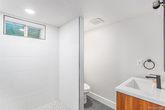 bathroom with a textured ceiling, tile patterned flooring, vanity, toilet, and tiled shower