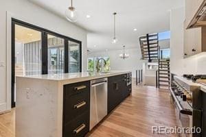 2620 N Perry St, Denver, CO 80212 - kitchen featuring stainless steel appliances, light countertops, light wood-style flooring, a center island with sink, and pendant lighting