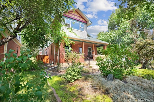 view of front of home featuring a porch, brick siding, and fence